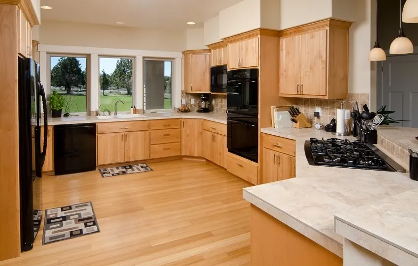 Modern kitchen with tile countertops cooktop utensils black appliances windows hardwood cabinets and floor and tile backsplash