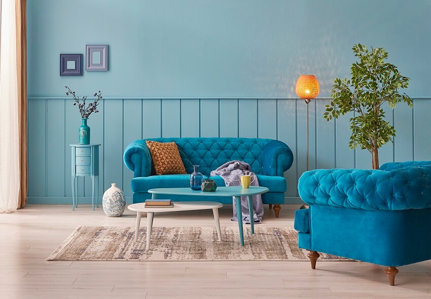 Modern living room with blue wall background blue velvet sofa and armchair orange lamp two coffee tables on carpet and vase of plant