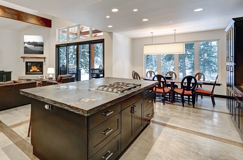 Modern open floor kitchen with dark wood island with honed granite countertop and view of the dining area and living room with fireplace and wood beam