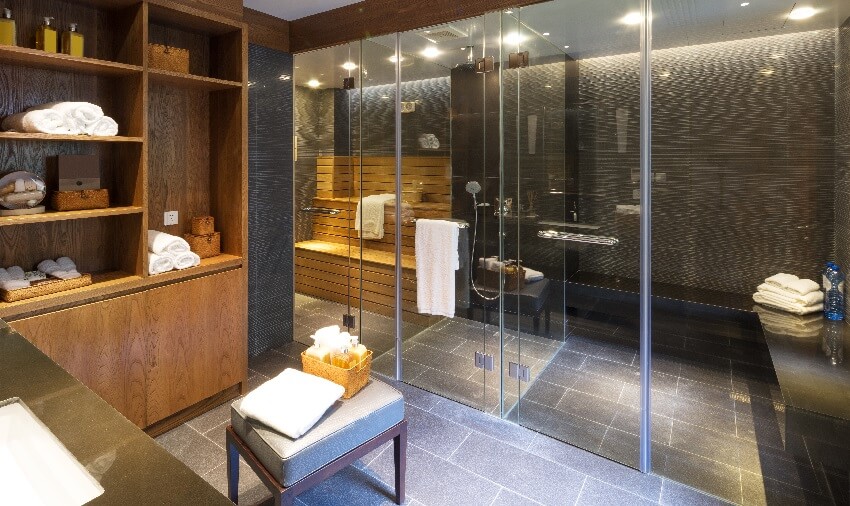 Modern sauna room with black tile floors wood cabinet and shelves a bench and an ottoman