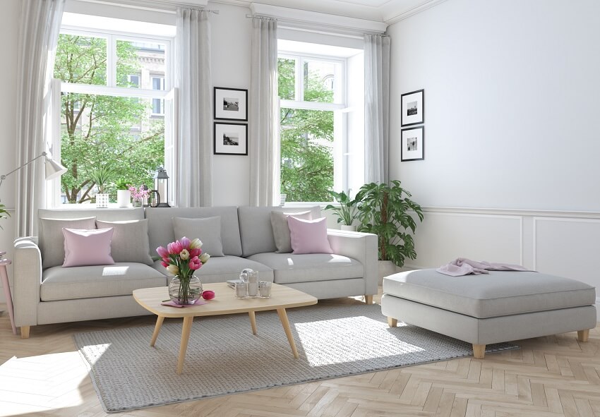 Modern townhouse living room with light wood coffee table grey sofa and ottoman windows with sheer curtains and rug with pad on hardwood parquet floor