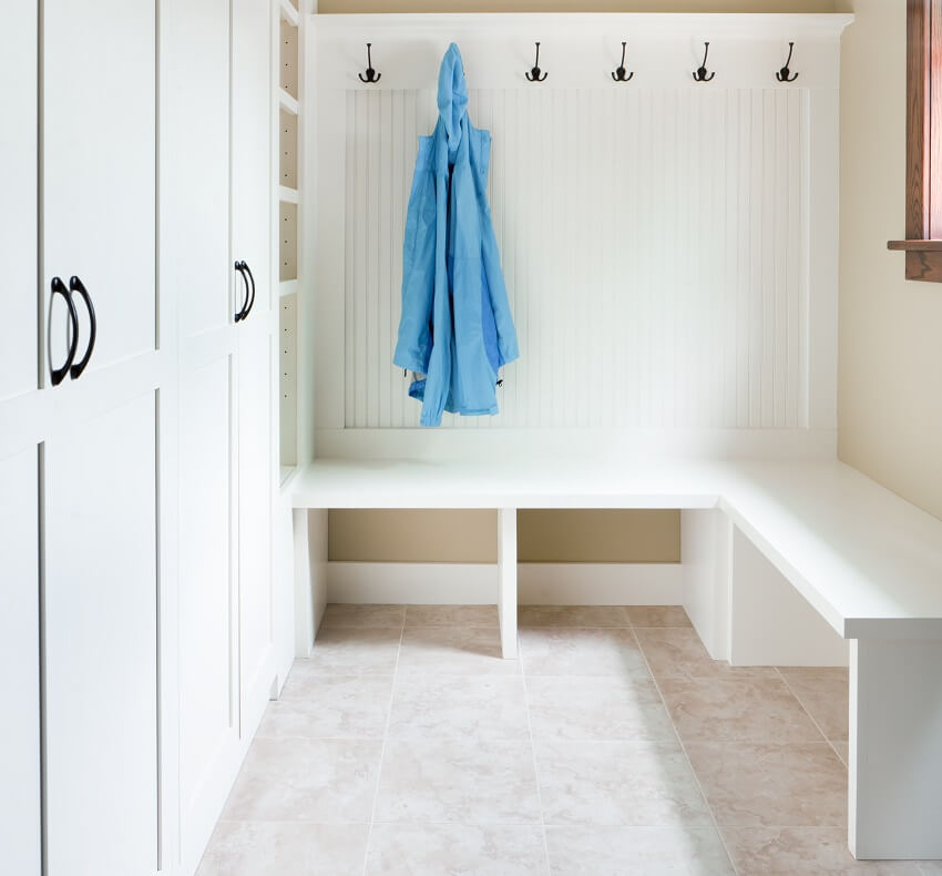 Mudroom space with built in furniture storage closets blue coat hanging from a hook shoes storage compartments under a seating bench and a porcelain tile flooring