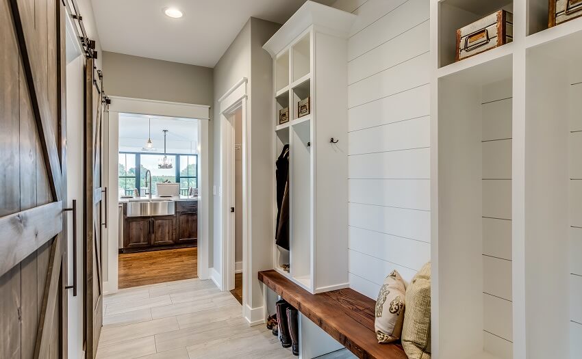 Mudroom with natural wood bench shiplap wall cubbyhole lockers tile floors and view of the kitchen with wood floors