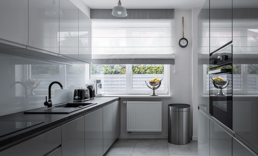 Narrow kitchen with pendant light tile floor grey and white cabinets black countertops stainless steel trash compactor and windows with white and grey shade