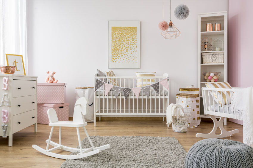Nursery room for girls with crib, wood floor, white wall, rug, pendant light, dresser, and window