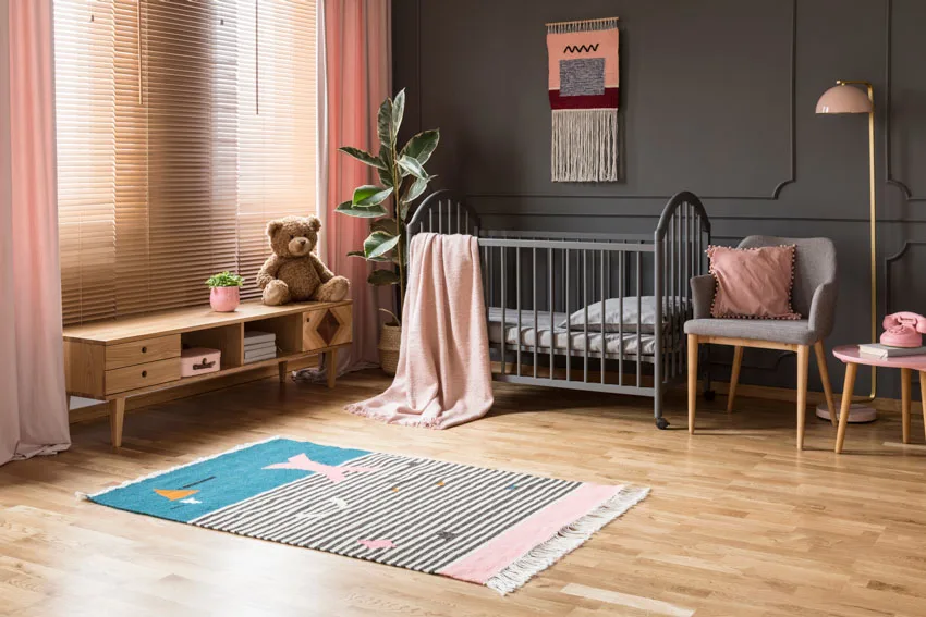 Nursery room for girls with gray paint color wall, wood floor, crib, chair, lamp, and sheer curtains