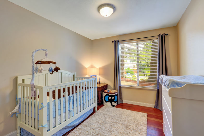 Nursery room with beige walls, window, crib, and curtains