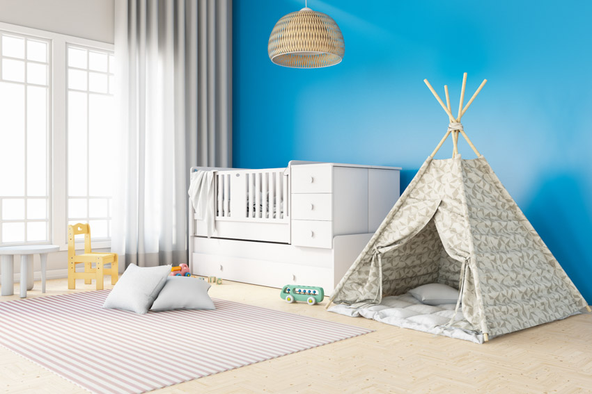 Nursery room with blue paint color, tent, crib, pendant light, and window
