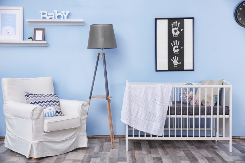 Nursery room with blue paint color wall, wood floor, crib, chair, and floor lamp