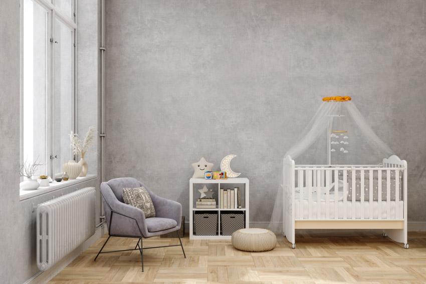Nursery room with gray concrete paint color, wood floor, crib, nightstand, chair, and windows