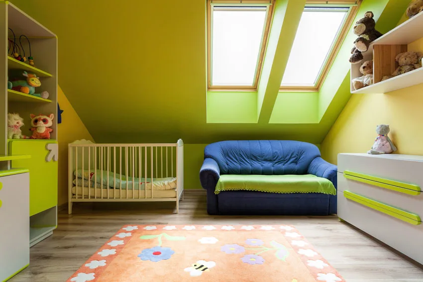 Nursery room with green paint color, crib, couch, cabinets, sloping ceiling, and skylight