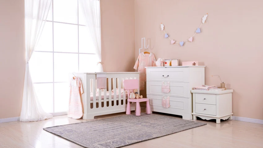 Nursery room with pink walls, crib, dressers, and windows