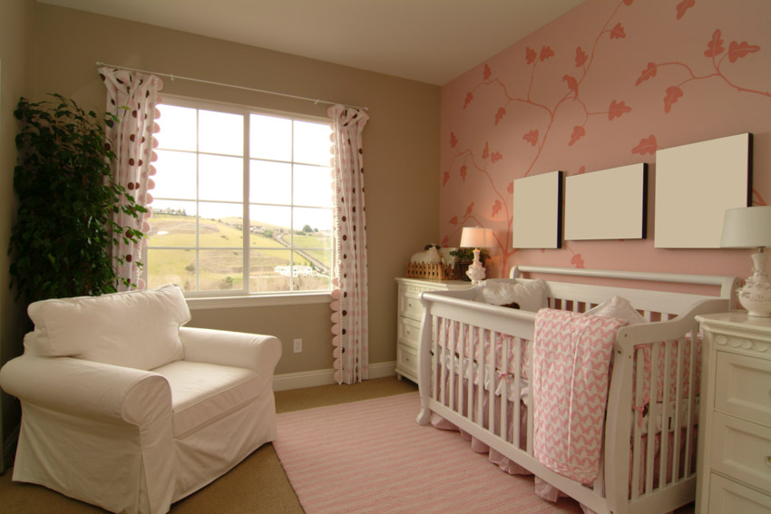 Nursery room with pink wall, crib, white chair, and window