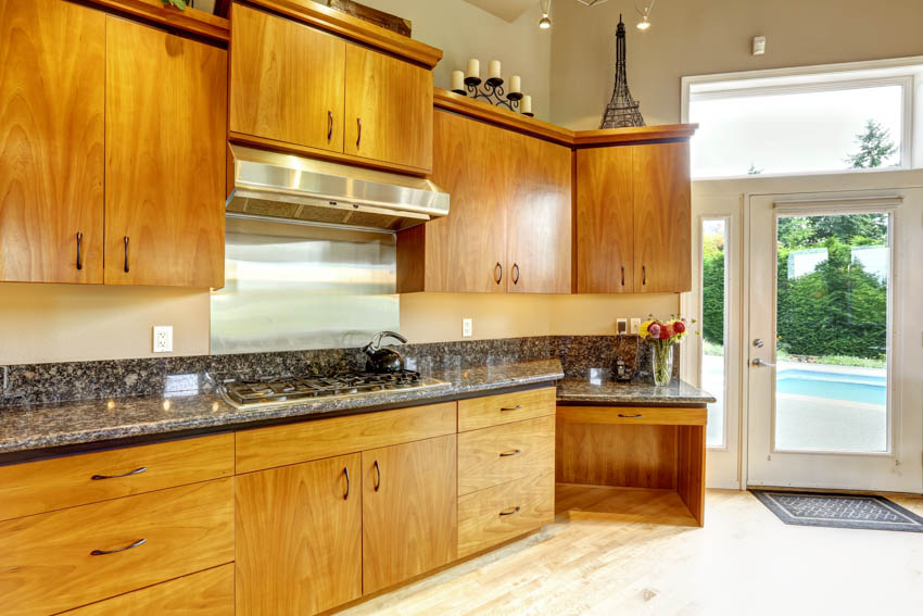 Kitchen with yellow honey hue oak cabinets, backsplash, countertop, flooring, hood, and glass door