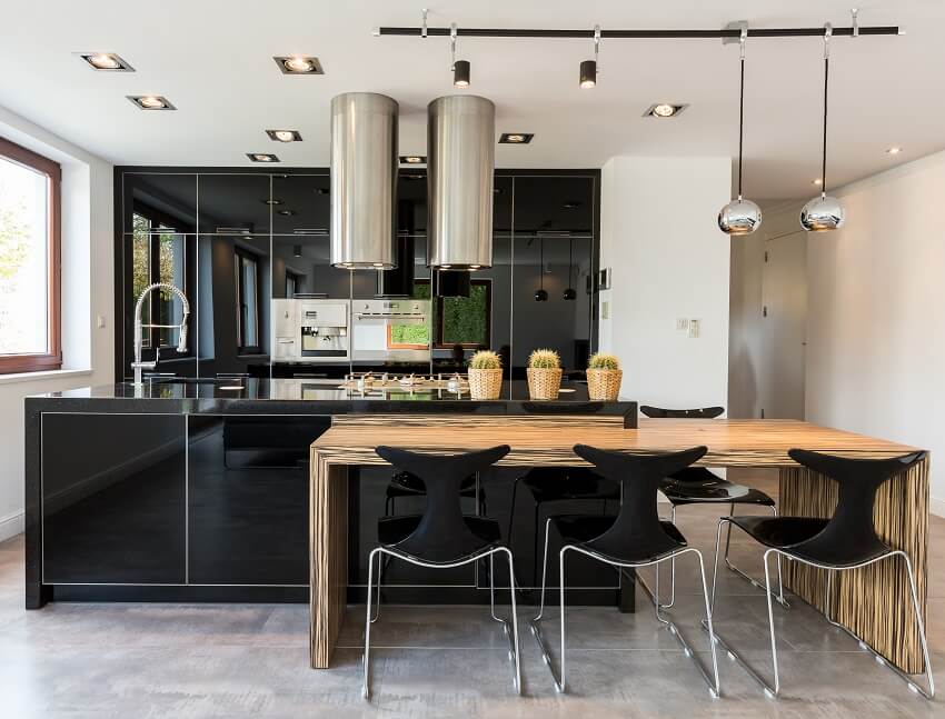 Open kitchen with black cabinets and two cylinder range hoods, gray tile floor and a wood dining table 