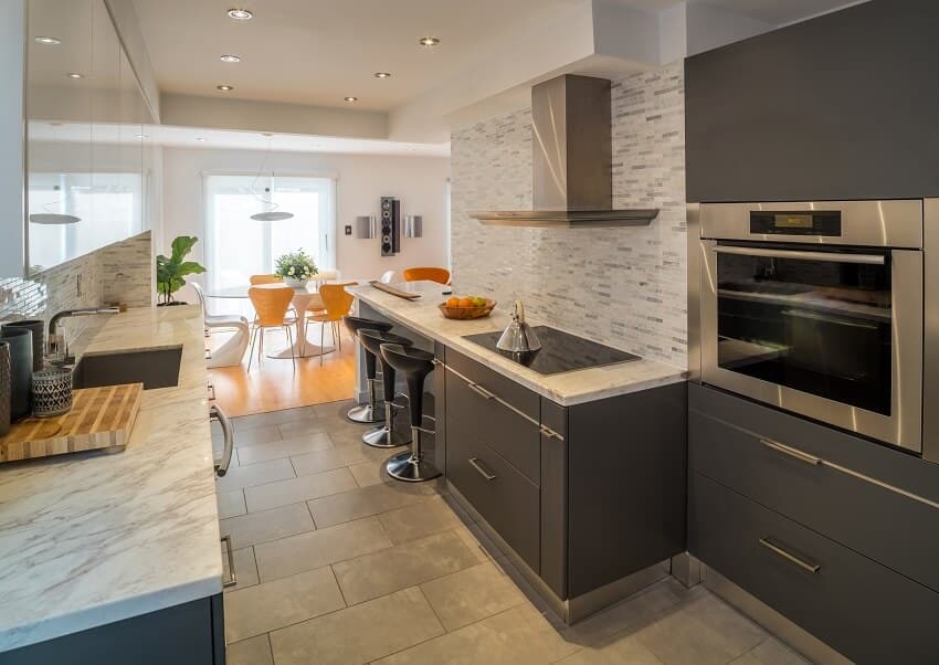 Open kitchen with grey cabinets quartz countertops mosaic backsplash grey slate brushed floors and view of the bright dining area