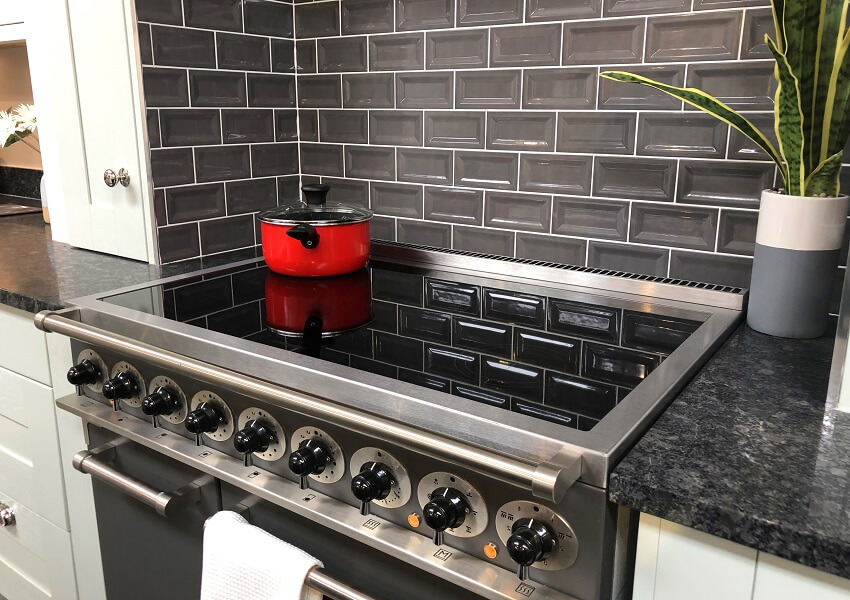 Part of a kitchen with a granite countertop glossy grey brick tiles backsplash white cabinet kitchen cooker stove with ceramic hob and touch control knobs