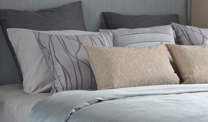 Pillows with patterned cases on bed with light blue satin blanket