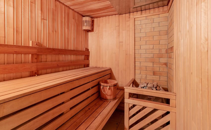 Sauna room with a bench hot stones a soft light and a brick accent wall in the corner