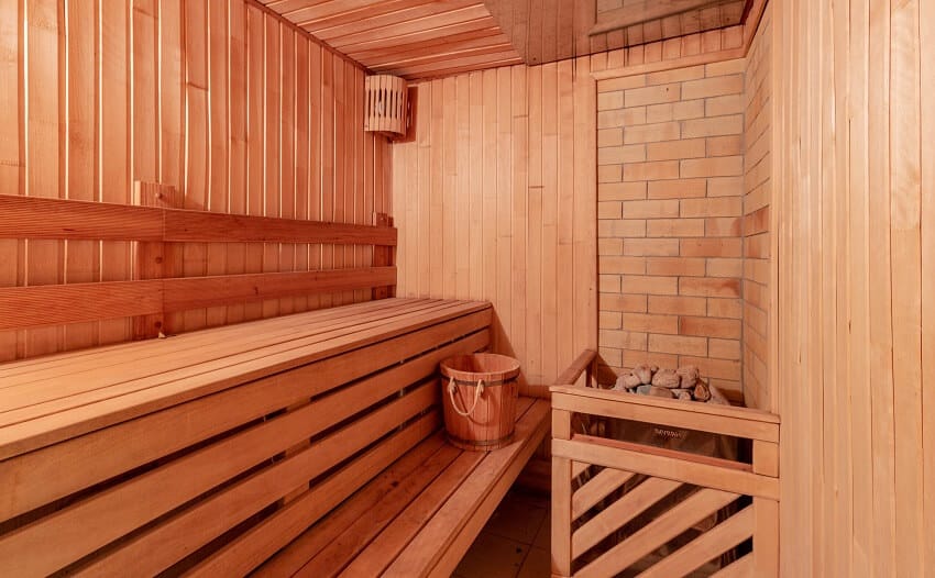 Sauna room with a bench, hot stones, a soft light, and a brick accent wall