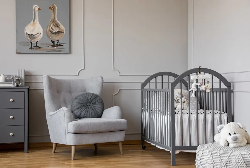 Simple nursery room with sofa chair, gray walls, crib, dresser, and wood floor