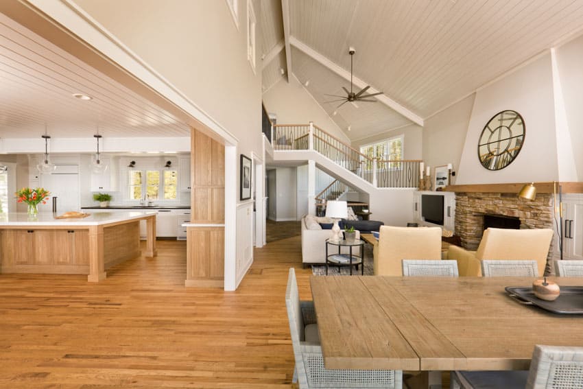 Spacious home interior with sloped shiplap types of wood ceiling, tables, chairs, center island, and fireplace