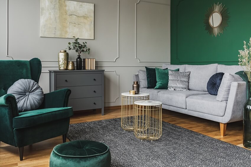 Stylish emerald green and grey living room interior design with abstract painting on the wall stylish table on carpet console table and velvet sofa and armchair
