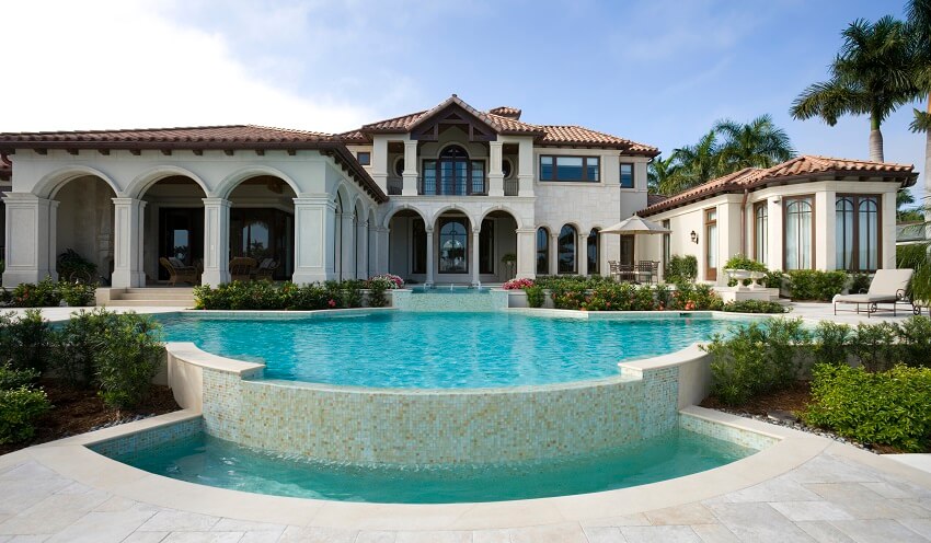Swimming pool with slate tile deck at a Mediterranean mansion with red tile roof and a balcony with French doors
