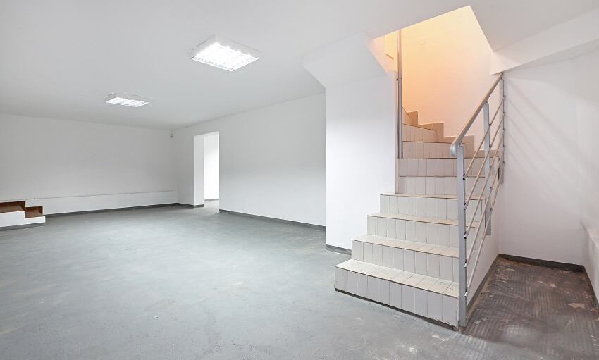 Tiled stairs to empty basement with white walls lighting fixtures and concrete floors
