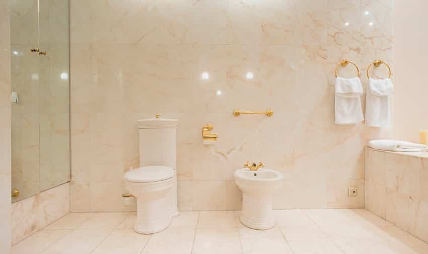 Toilet interior with marble tile floor and walls cabinet with mirror doors and towels hanging in brass towel ring