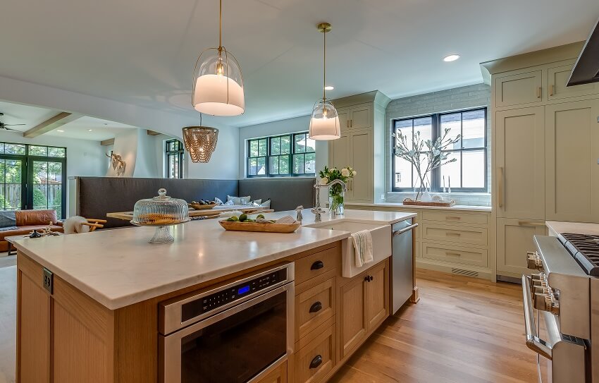 Two pendant lights hang above island with marble countertops sink and microwave drawer in an open kitchen with hardwood floors and wood dining table