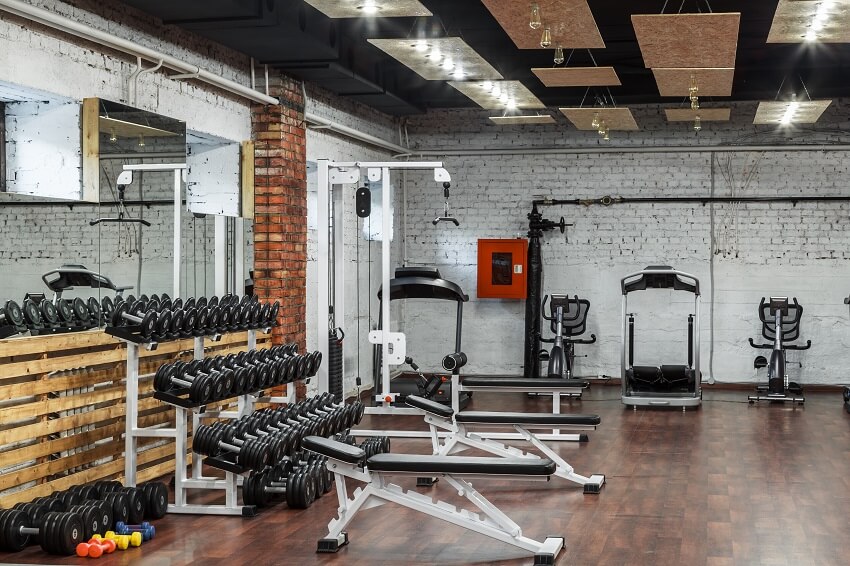 Underground gym with equipment brick wall and column mirror hardwood floor and hanging panels with light bulbs
