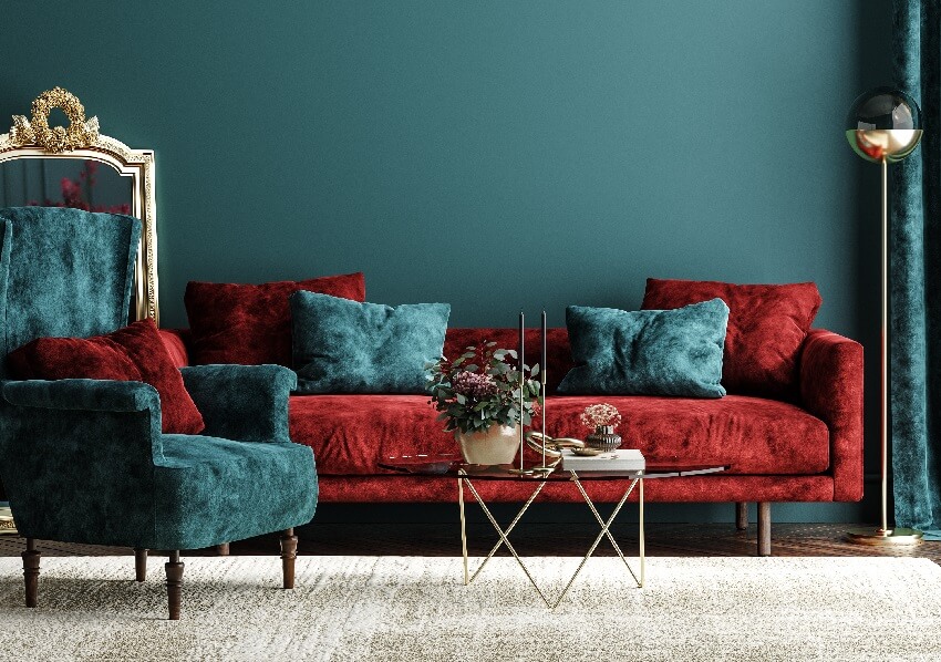 Velvet red sofa and blue green armchair with throw pillows in a living room with glass coffee table floor lamp and white carpet