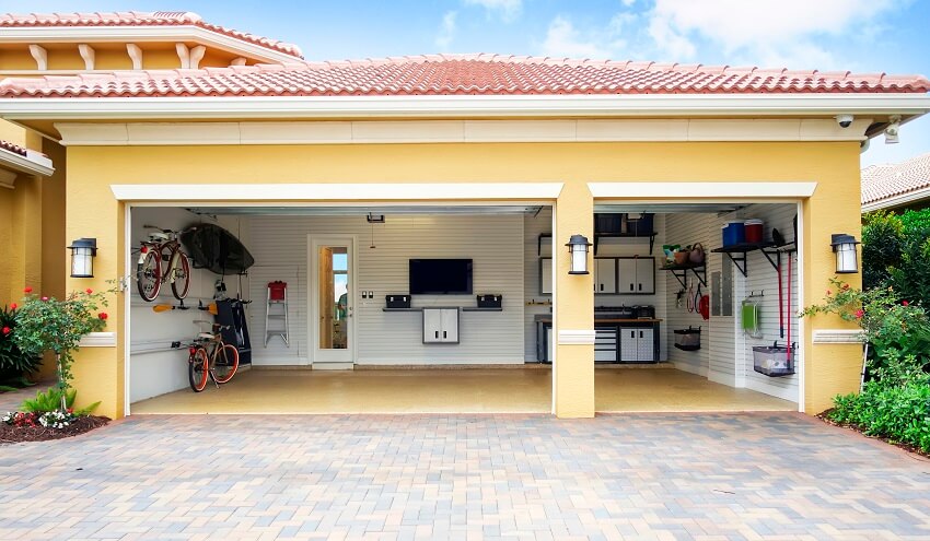 Well organized three car garage attached to a home with shiplap walls shelves bicycle racks work area storage cabinets and a flat screen tv on the wall