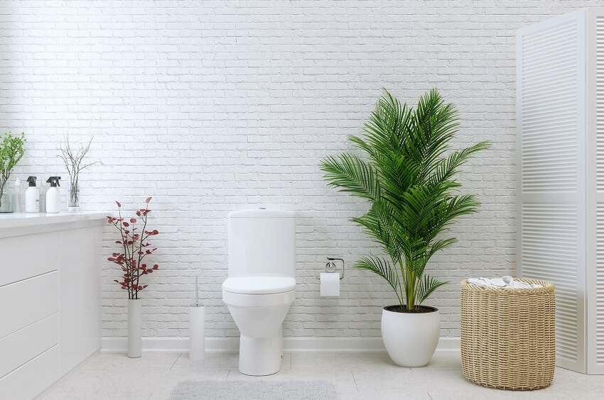 White bathroom with indoor plants brick wall rattan basket divider tile floor and an upflush toilet