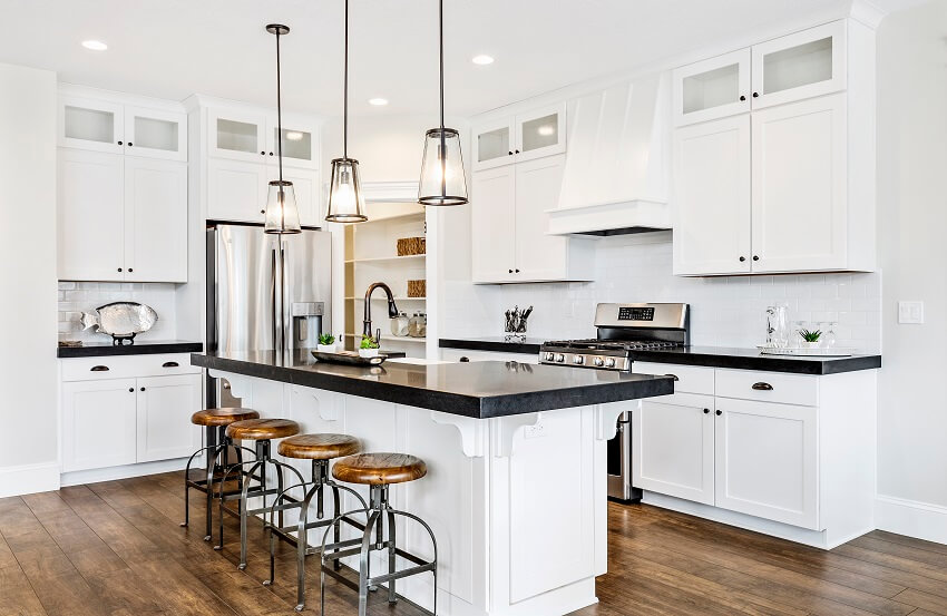 White gourmet kitchen with black countertops pendant lights stainless steel appliance wood floors subway tile backsplash and an island with stools