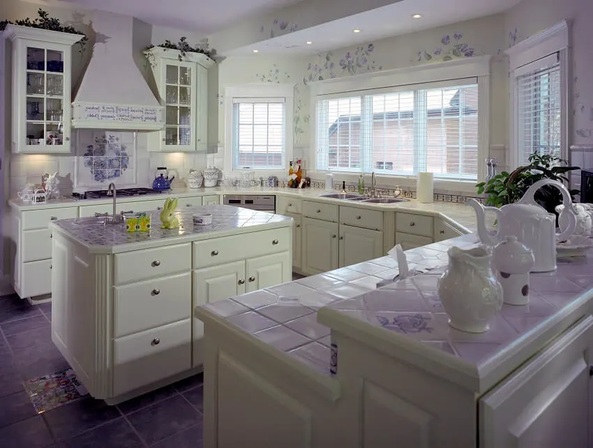 White kitchen with tile countertops and floor flower printed walls and ceilings white cabinets island and windows with blinds
