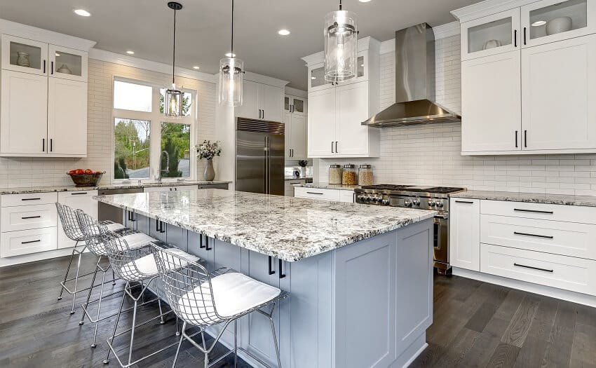 White kitchen wood floor brick backsplash and large island with polished granite countertop stainless steel chairs and pendant lights hanging over