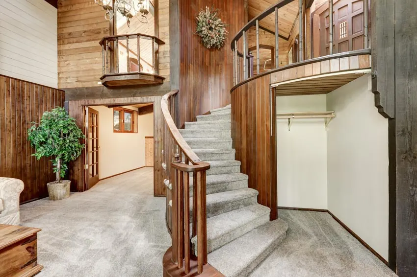 Vertical wood decoration by the winding staircase, marble flooring, and wreath decor