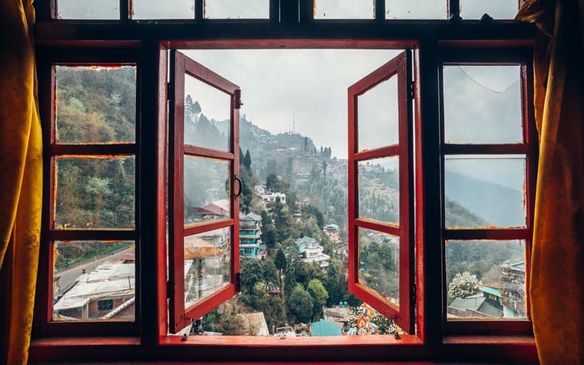 Wooden double casement window with curtains overlooking a mountain village