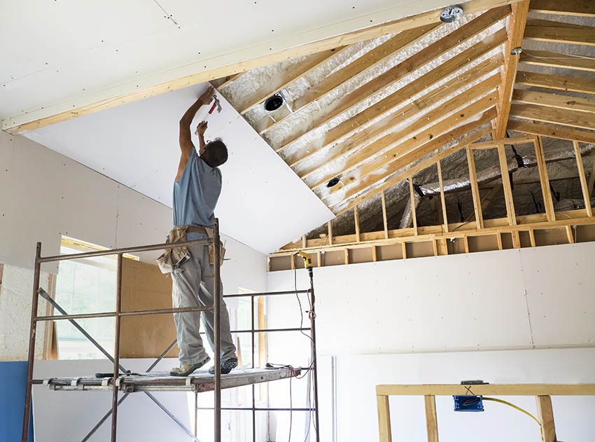 Worker hanging drywall on ceiling