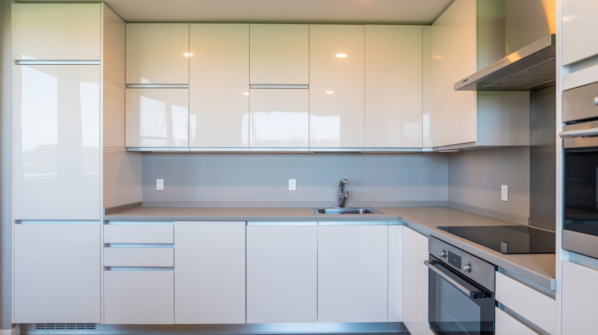 Compact kitchen with glossy white thermofoil slab cabinets and blue tile backsplash
