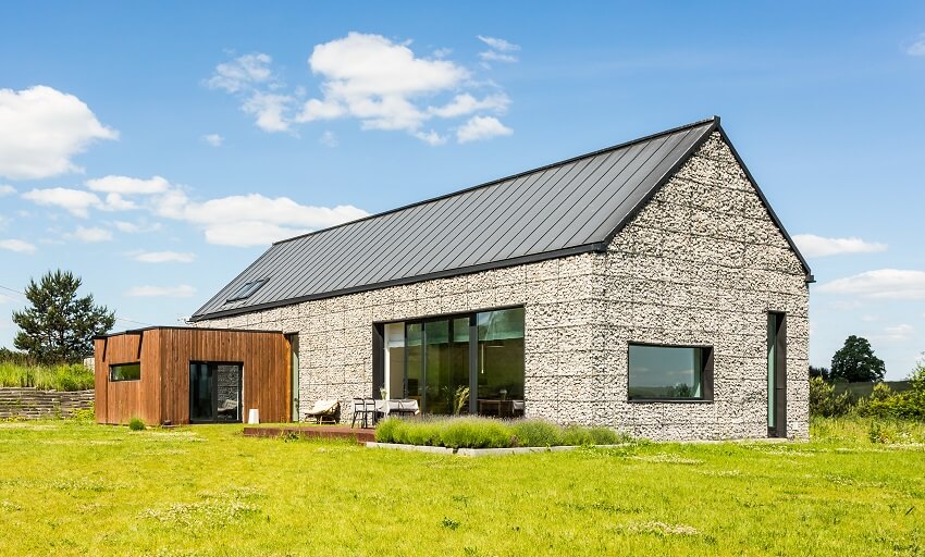 A barndominium with a concrete facade, black metal roof, and skylight window