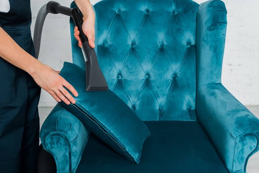 A cleaner dry cleaning a throw pillow on a blue velvet armchair