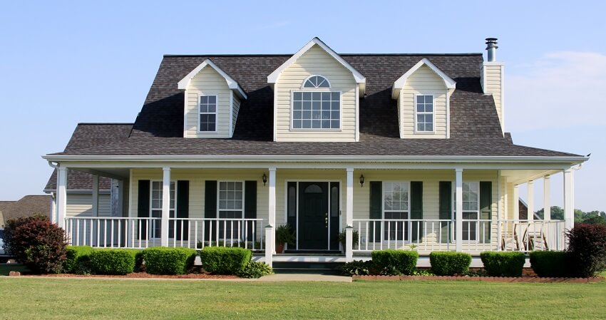 A country farmhouse with shingle roofing, front porch, shiplap siding, and manicured lawn