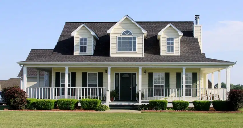 A country farmhouse with shingle roofing with front porch and manicured lawn