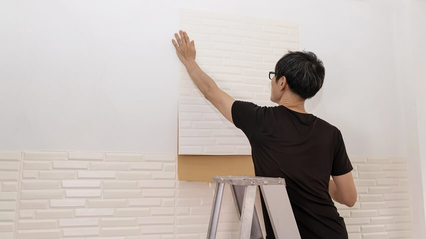 A man putting up wallpapers on the wall of a room