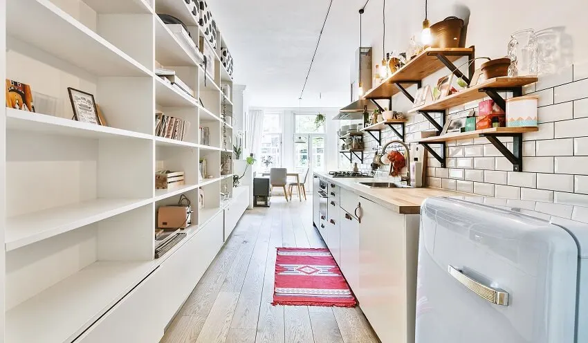 A narrow kitchen with pantry with pendant lights, subway tile backsplash, and decors on wooden floating shelves
