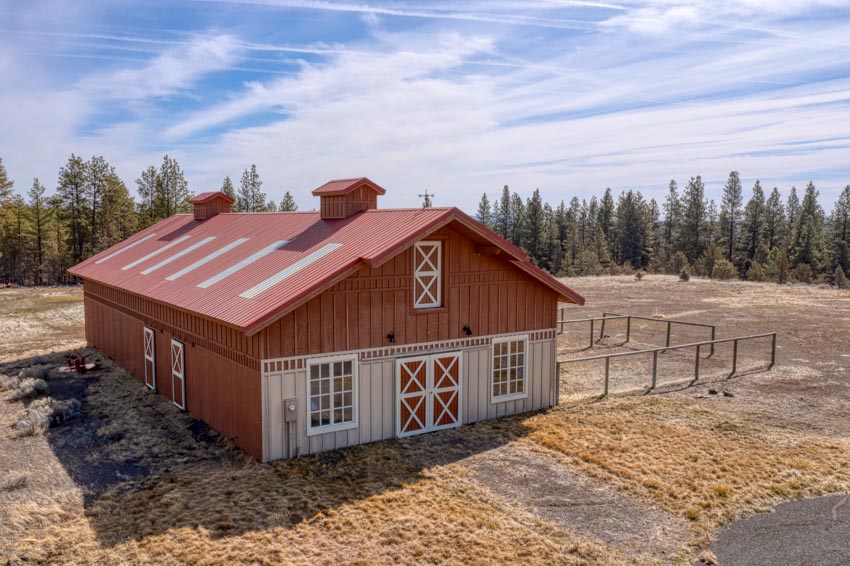 Aerial view of red barndominium with white windows, pitched metal roof, and cupolas