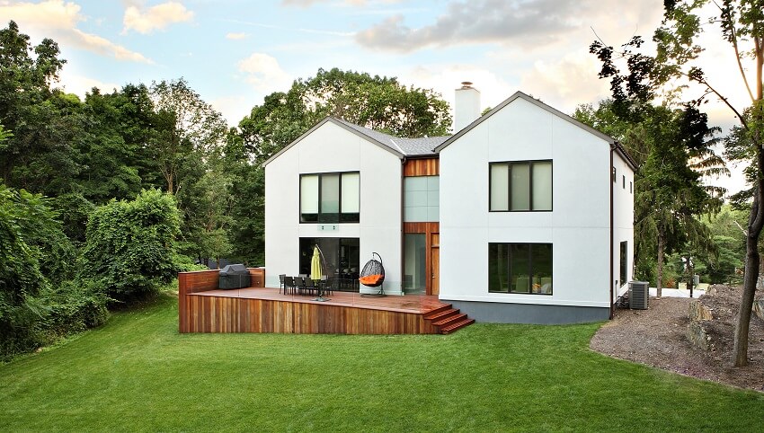 Backyard of a white facade barndominium with chimney, deck, and manicured lawn